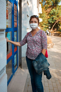 Woman standing at front of pharmacy, wearing face mask to cover mouth and nose during pandemic