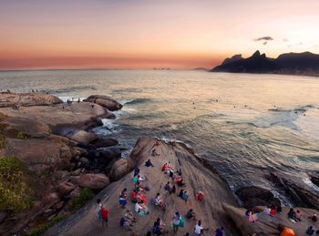 High angle view of people on rock formations by sea at arpoador during sunset