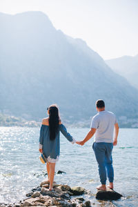 Rear view of couple holding hands while standing on rocks in sea