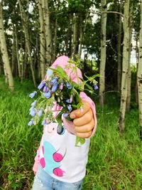 Midsection of woman holding flowering plant in forest