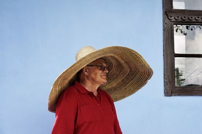 Senior man wearing large hat standing against blue wall