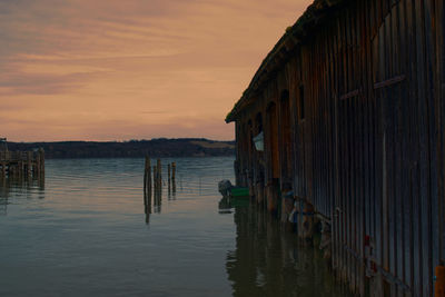 Wooden posts in sea against sky during sunset