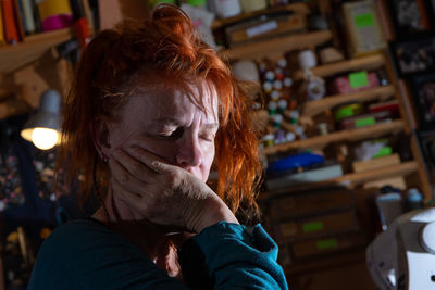 A depressed woman sits in a room. she supports her head in her hands and has her eyes closed.