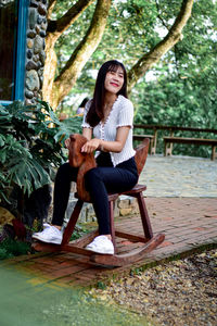 Smiling young woman sitting on rocking horse outdoors