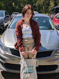 Portrait of young woman standing by car