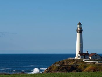 Lighthouse by sea against clear blue sky