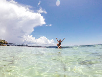 Woman sitting on rock in sea against blue sky