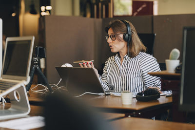 Mature businesswoman wearing headphones while talking on mobile phone in office