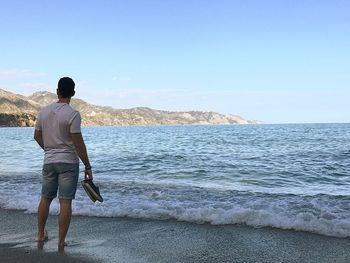 Rear view of man standing on beach against sky