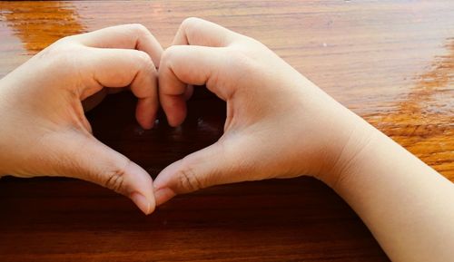 Cropped hands of woman forming heart shape on table