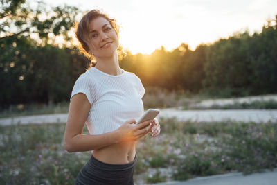 Young woman using smart phone against sky during sunset