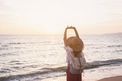Woman standing at beach against sky during sunset