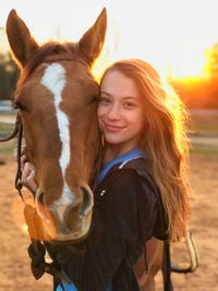 Portrait of smiling teenage girl embracing horse during sunset