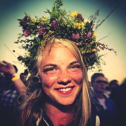 Portrait of smiling young woman wearing flowers against sky