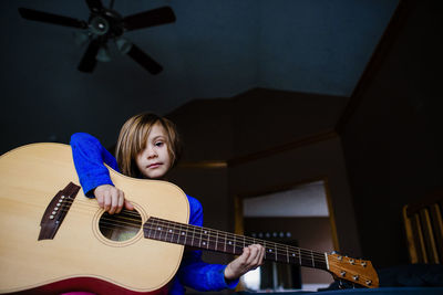 Low angle portrait of girl playing guitar while sitting at home