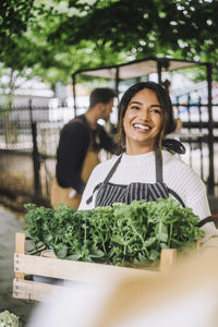 Happy female florist holding crate of plants during festival at market