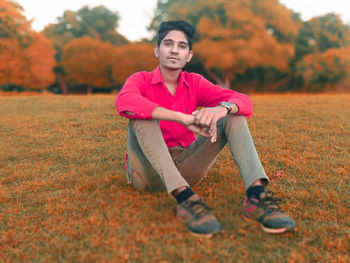 Portrait of young man sitting on seat during autumn