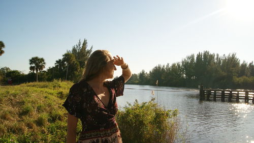 Woman shielding eyes while standing by lake on field