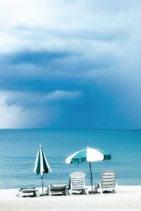 Deck chairs on beach against sky