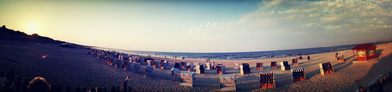 sky, built structure, sea, architecture, beach, travel destinations, tourism, cloud - sky, vacations, in a row, water, sunset, sunlight, outdoors, horizon over water, building exterior, parasol, large group of people, panoramic, nature