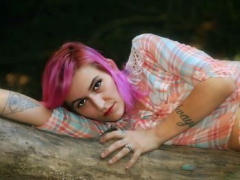 Portrait of young woman with dyed hair lying on log in forest