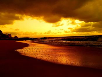 Scenic view of beach against dramatic sky during sunset