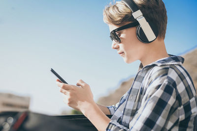 Side view of boy using smart phone against sky