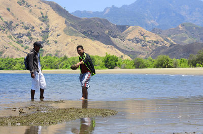 Full length of friends standing by lake against mountains