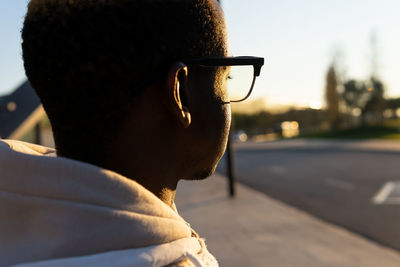 Side view of crop unrecognizable african american male on stylish sunglasses while standing on sunny street in city with buildings