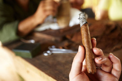 Cropped hand holding lit cigar at table