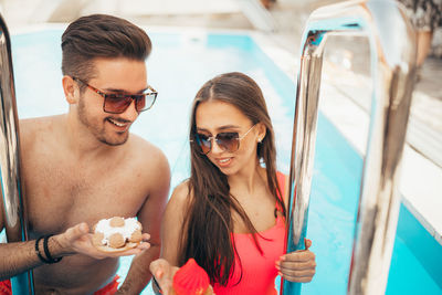 Young beautiful couple eating cookies by the pool