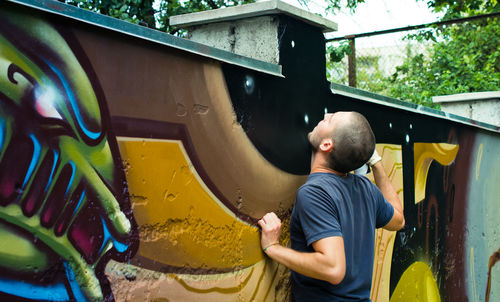 Rear view of young man spray painting on surrounding wall