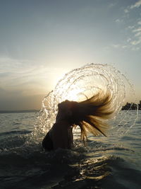 Side view of woman tossing hair in lake against sky during sunset