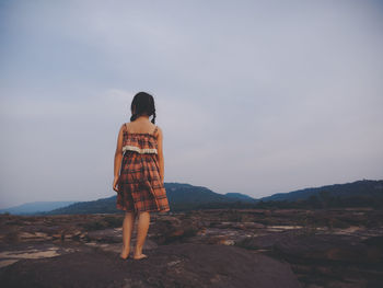 Rear view of girl standing on mountain against sky