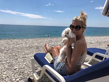 Portrait of smiling with dog sitting on lounge chair at beach