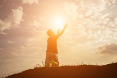 Side view of silhouette man with arms raised standing on mountain against sky during sunset