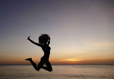 Woman jumping in sea at sunset