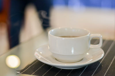 Hot coffee and tea in white ceramic cup on plate with smoke in blurry background.