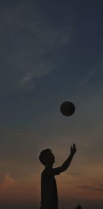 Silhouette boy playing with ball against sky during sunset