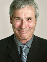 Close-up portrait of smiling senior man against gray background