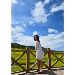 Woman standing on railing against sky