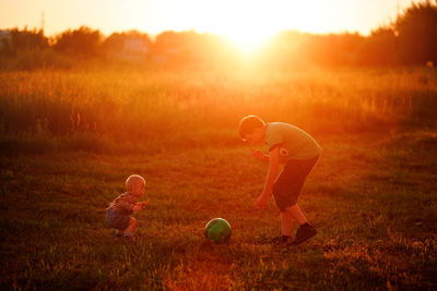 Boy plays ball with his younger brother at sunset