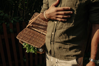 Midsection of man with hand on chest carrying picnic basket