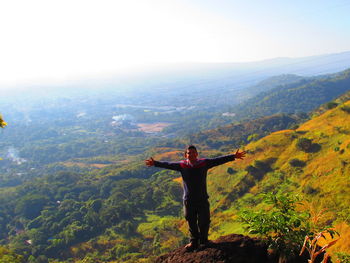 High angle view of young man with arms outstretched against landscape