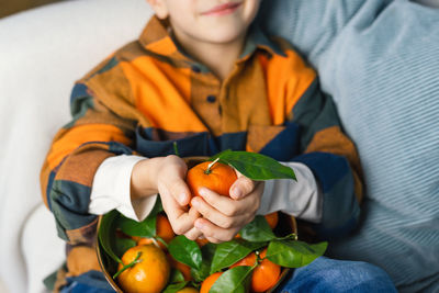 Close view of the hands of a child holding a tangerine. bright colors.