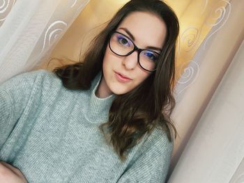 Portrait of young woman by curtain at home