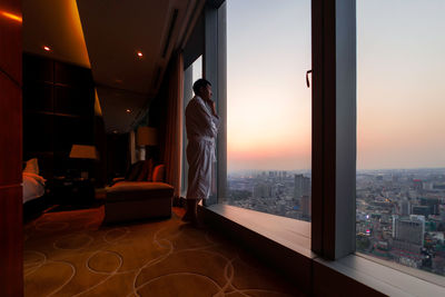 Buildings in city against sky during sunset seen through window