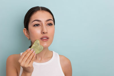 Portrait of young woman holding apple against blue background