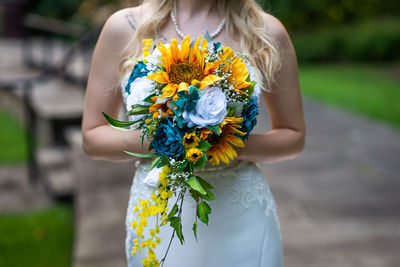 Midsection of woman holding bouquet while standing outdoors