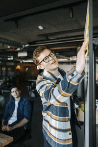 Businessman sticking adhesive notes on whiteboard while conducting meeting in office